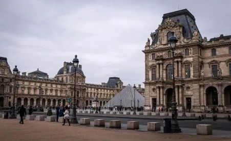 A striking view of the Louvre Museum's iconic glass pyramid entrance, surrounded by the historic palace architecture and vibrant sky, with visitors exploring the courtyard.